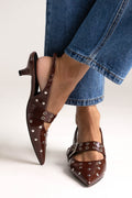 Burgundy patent studded slingback kitten heels with buckle strap, side view on a model in jeans