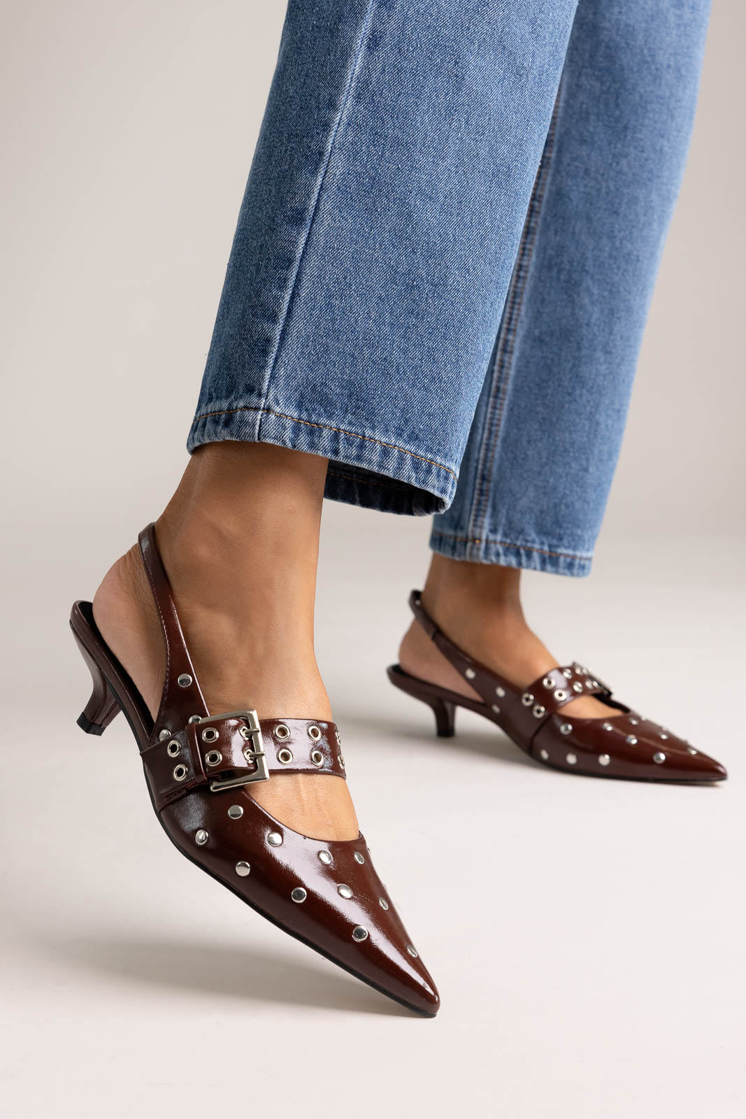 Burgundy patent leather pointed-toe kitten heel slingbacks with studs and buckle strap, angled view on a model