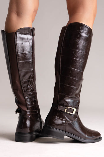 Dark brown croc-embossed knee-high riding boots with gold buckle strap and flat sole, rear view on a model