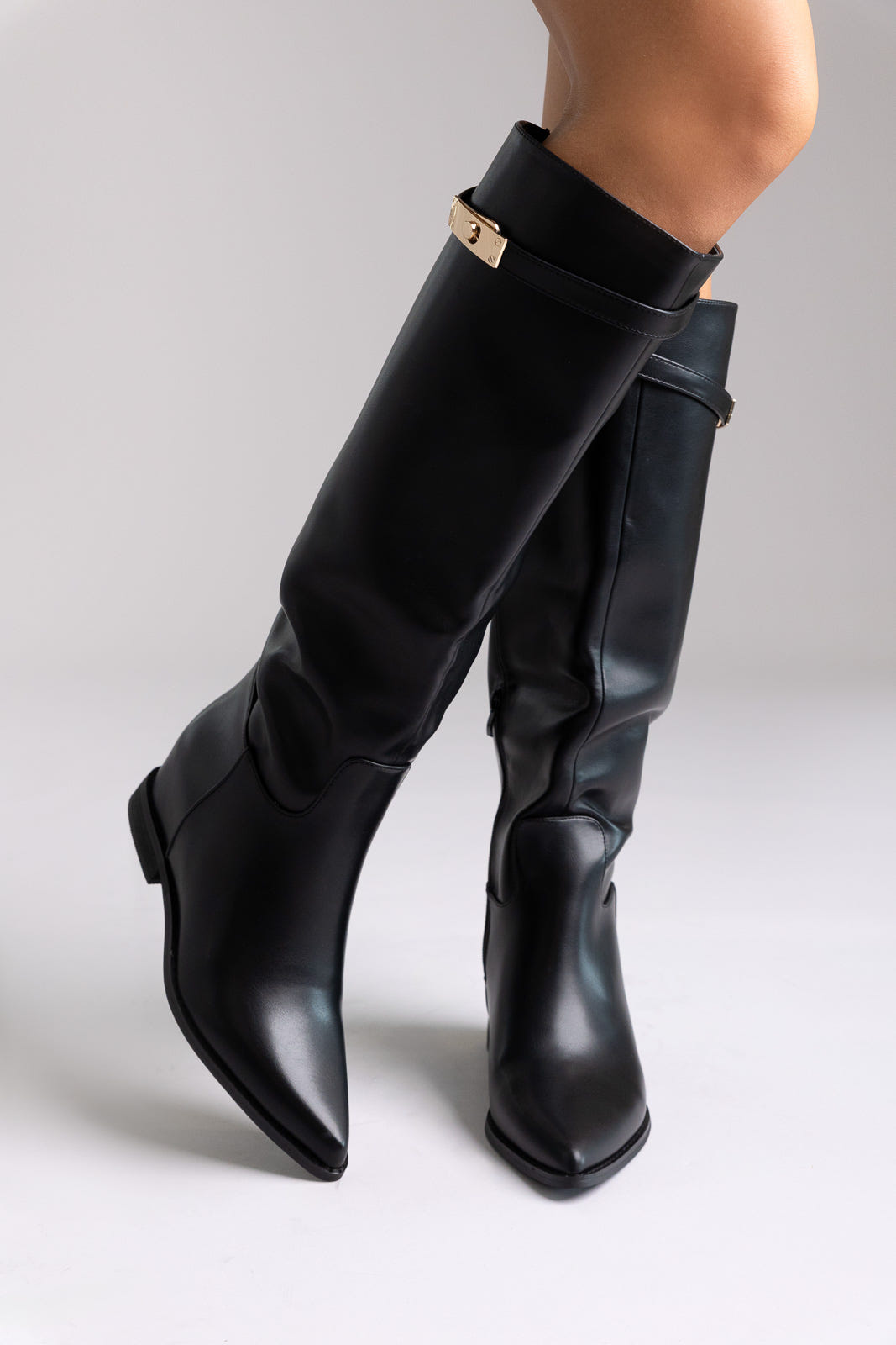 Black leather knee-high boots with gold buckle detail and block heel, angled view on a model