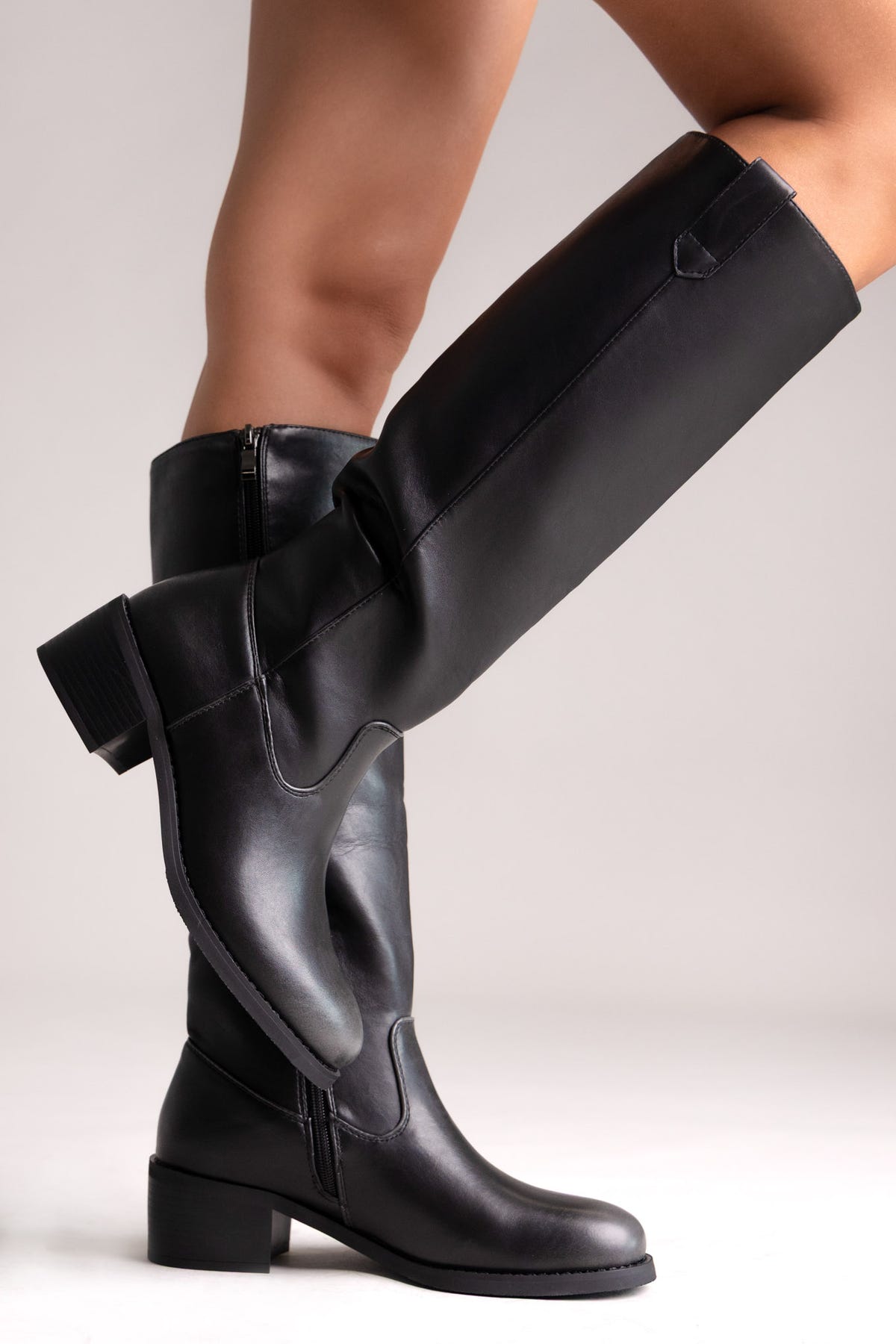Model leg in black leather knee-high boot with buckle detail and chunky block heel, angled view on a light background