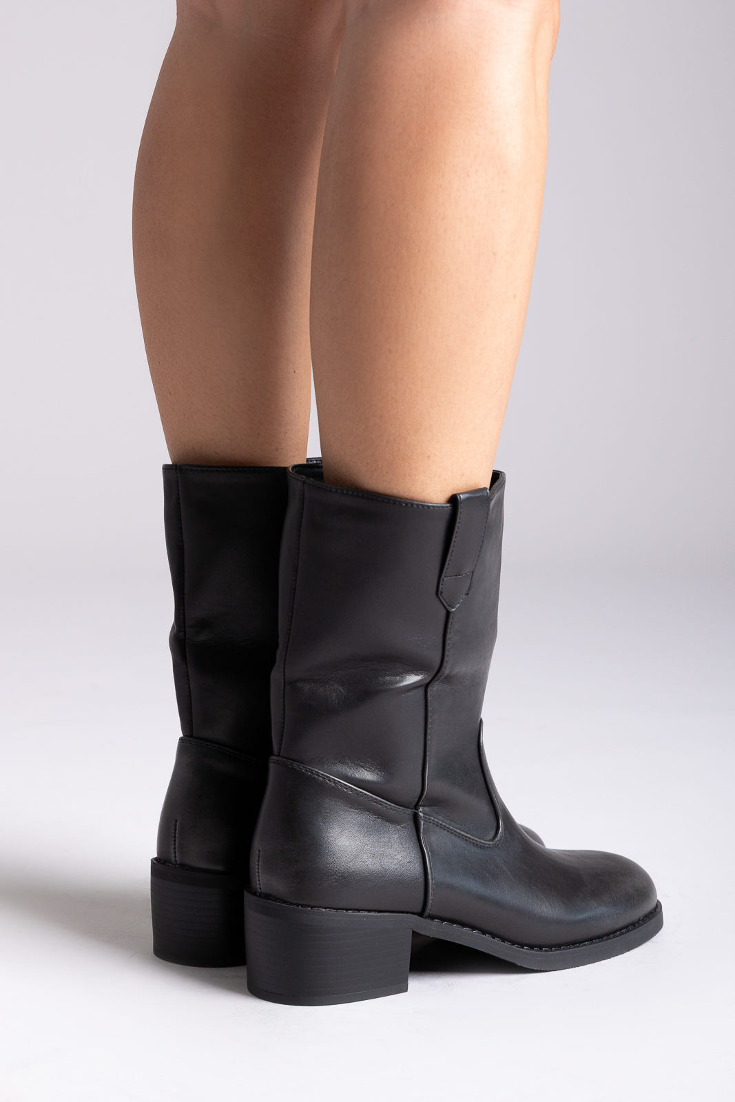 Black leather mid-calf boots with block heel and side panel, pair in front view on a model's legs in studio light