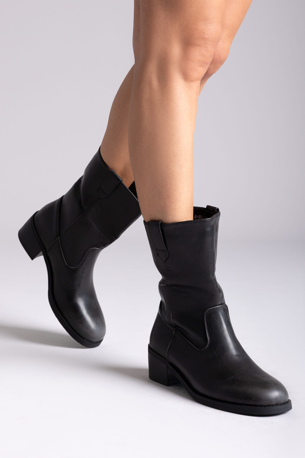 Black leather mid-calf boots with block heel and elastic side panel, angled view on a model's legs in studio light
