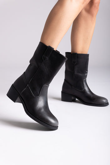 Black leather mid-calf boots with block heel and side panel, pair in angled view on a model's legs in studio light