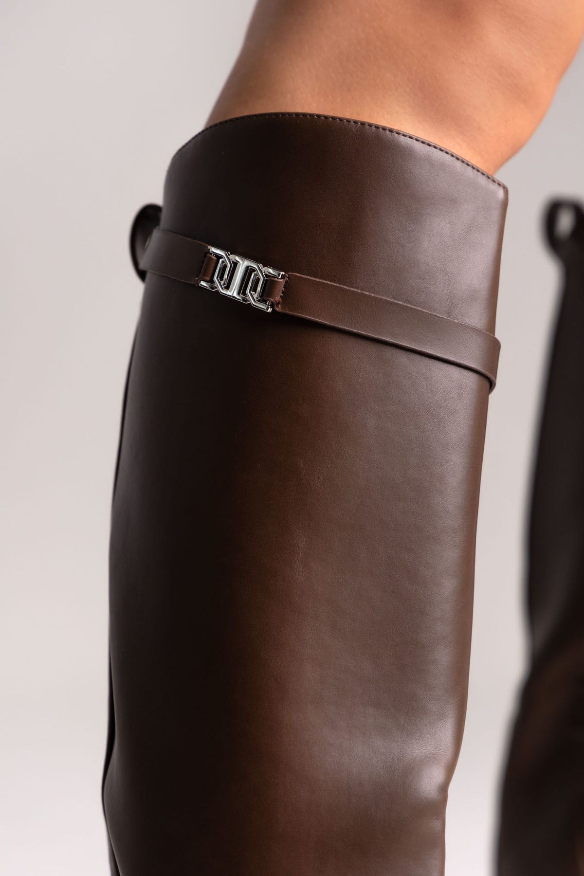 Brown leather knee-high riding boots with silver buckle strap and flat sole, side view on a model