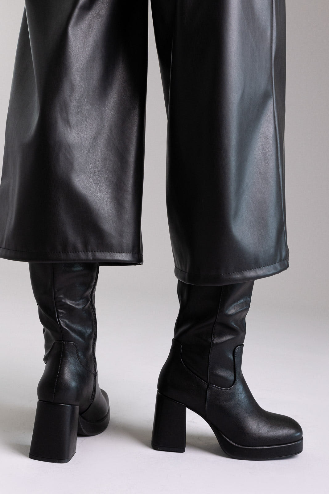 Model legs in black knee-high platform block heel boots with wide leg black trousers, front view on light grey