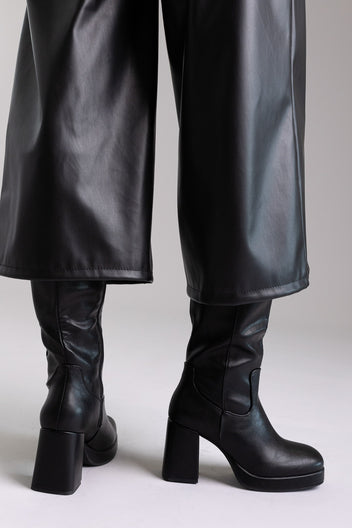 Model legs in black knee-high platform block heel boots with wide leg black trousers, front view on light grey