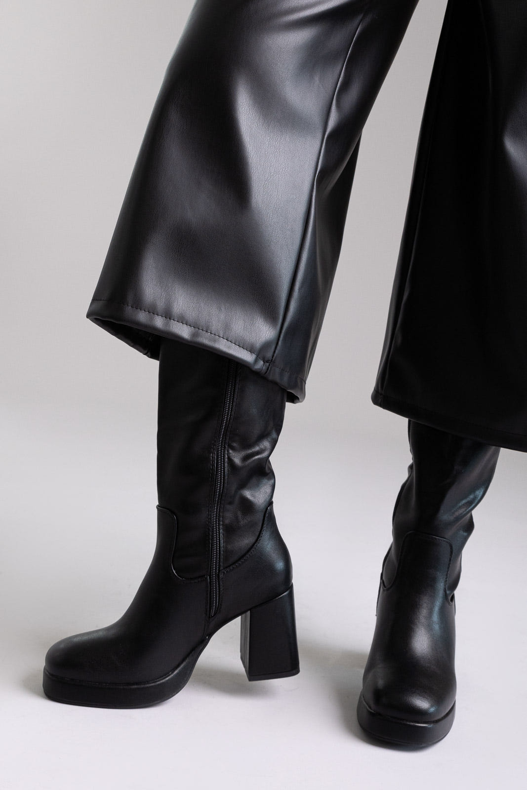 Model legs in black knee-high platform block heel boots with wide leg black trousers, front view on light grey
