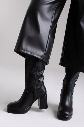 Model legs in black knee-high platform block heel boots with wide leg black trousers, front view on light grey