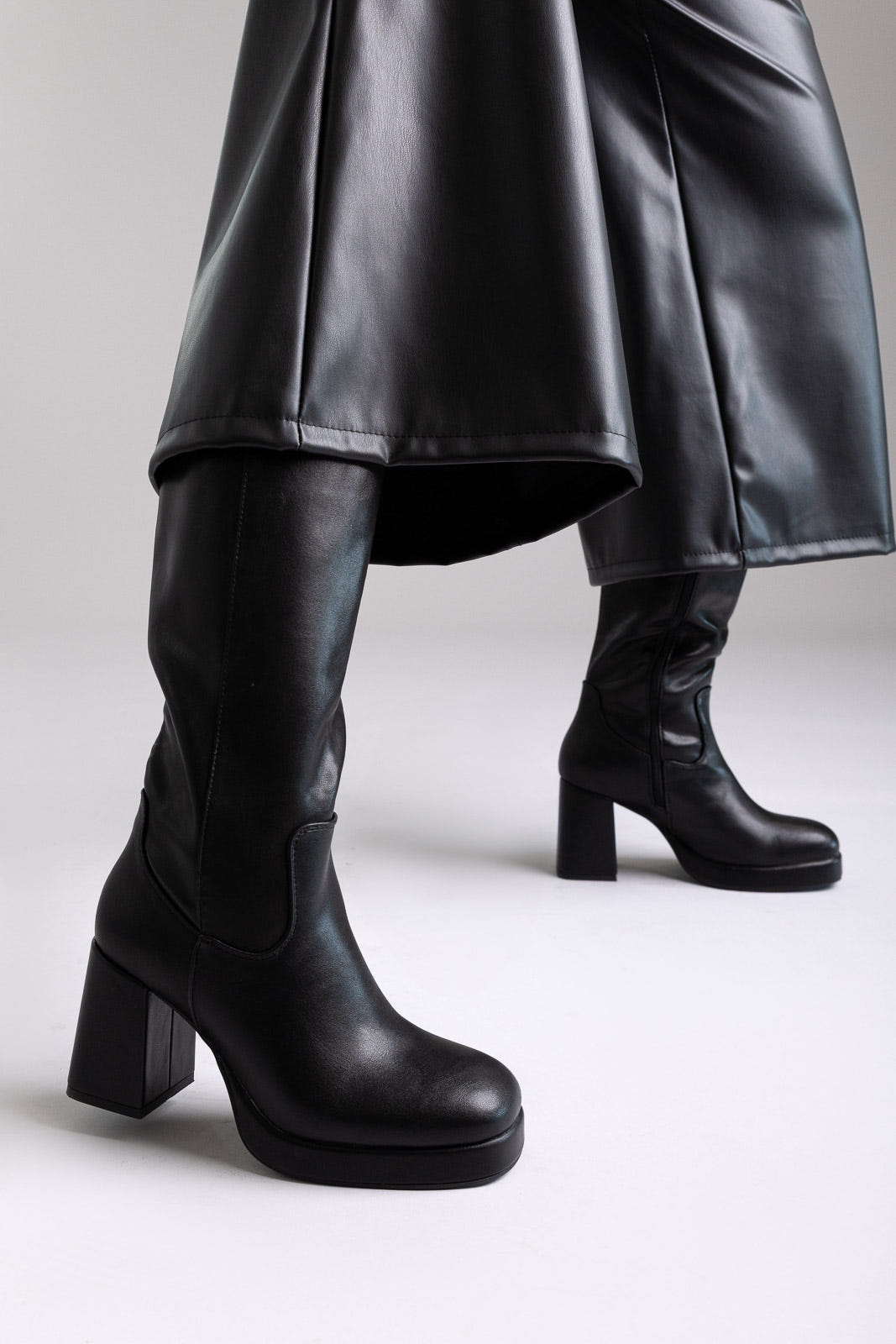 Model legs in black knee-high platform block heel boots with wide leg black trousers, side view on light grey