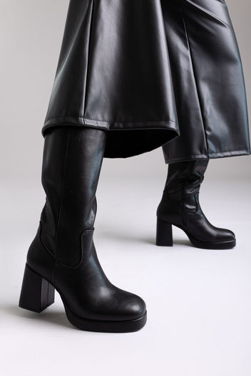 Model legs in black knee-high platform block heel boots with wide leg black trousers, side view on light grey