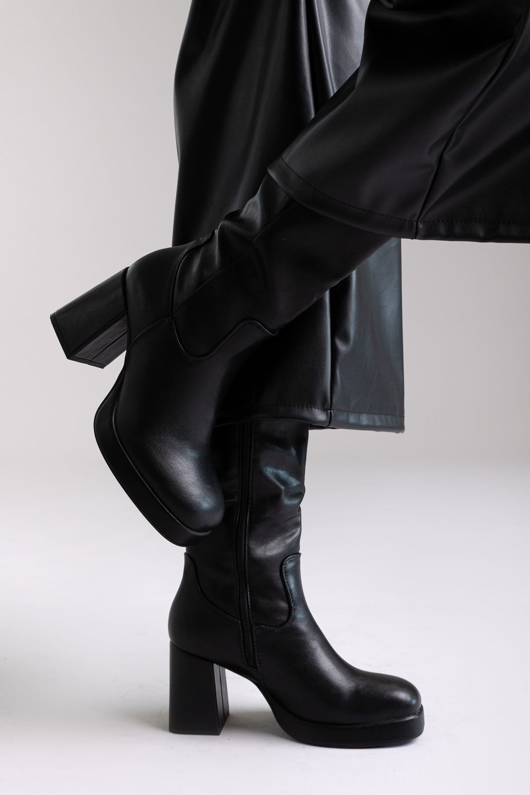 Model legs in black knee-high block heel boot with lug sole and side zip, angled view on light grey background