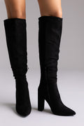 Black suede over-the-knee boots with pointed toe and block heel, standing side by side on light backdrop