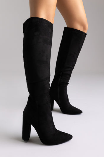 Black suede over-the-knee boots with pointed toe and block heel, close-up of legs on white backdrop