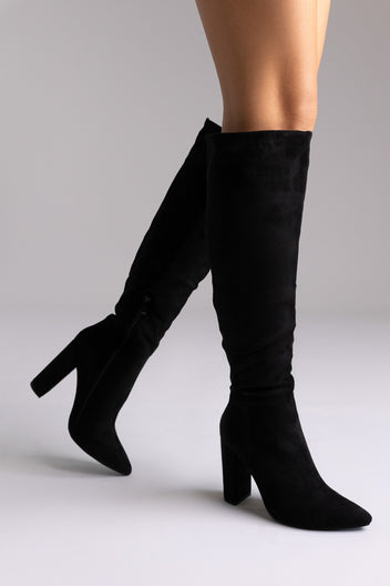 Black suede over-the-knee boots with pointed toe and block heel, side view on white backdrop