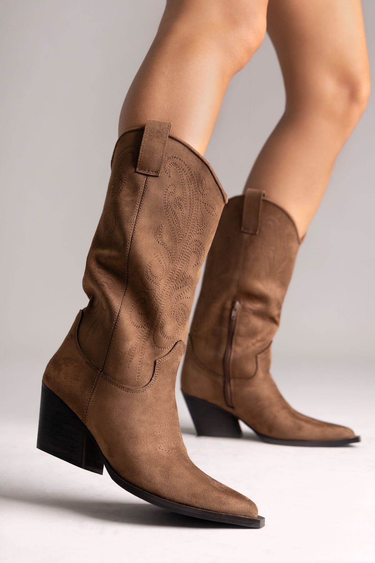 Tan faux suede embroidered western knee-high boots with stacked heel and pointed toe, angled view on a model