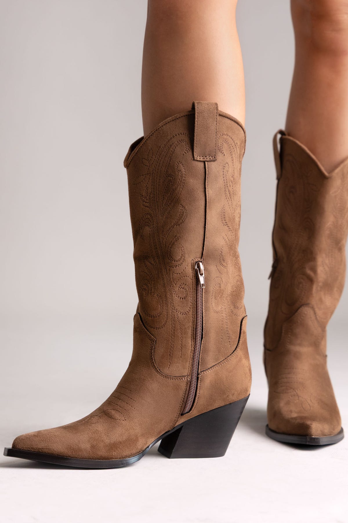 Tan faux suede embroidered western knee-high boots with stacked heel and pointed toe, side view on a model