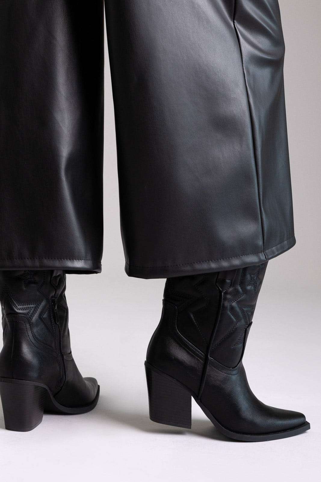 Black faux leather knee-high western boots with block heel and stitched shaft, angled view on a model