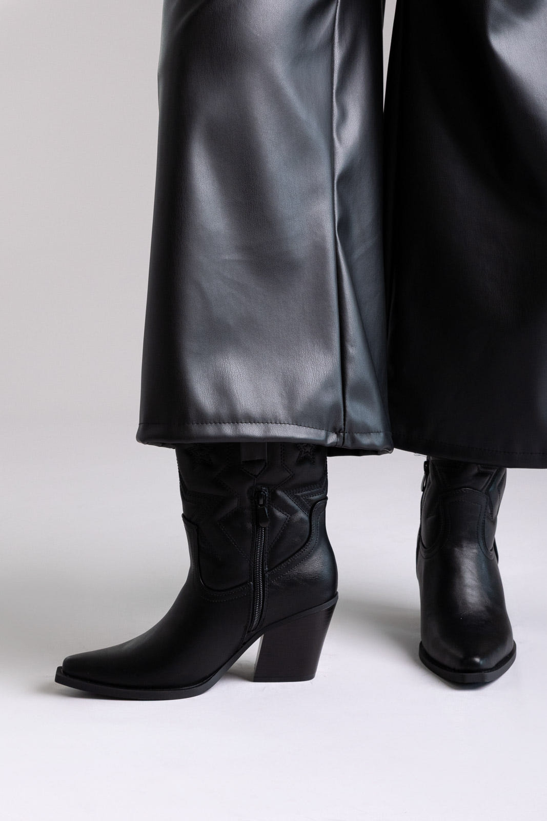 Black faux leather knee-high western boots with block heel and stitched shaft, close-up view on a model
