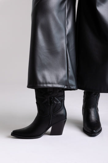 Black faux leather knee-high western boots with block heel and stitched shaft, close-up view on a model