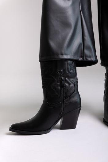 Black faux leather knee-high western boots with stacked heel and stitched shaft, angled view on a model