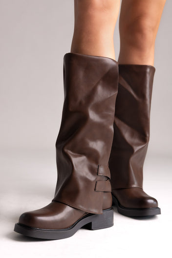 Pair of brown leather knee-high boots with buckle straps and chunky sole, angled view on a light grey background