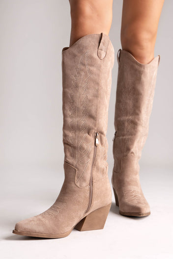 Taupe suede knee-high western boots with stitched shaft detail and pointed toe, side view on a model