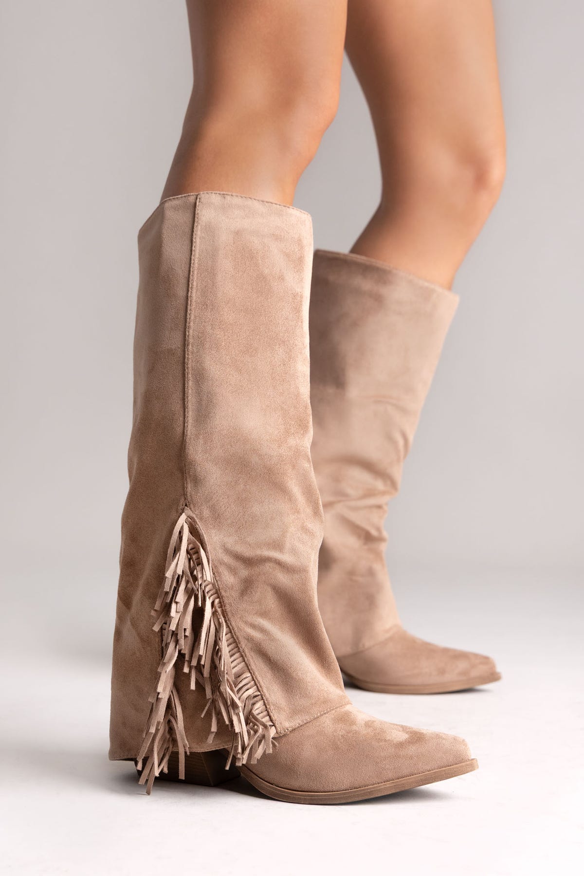 Taupe suede fold-over knee-high boots with fringe trim on the cuff, front angled view on a model