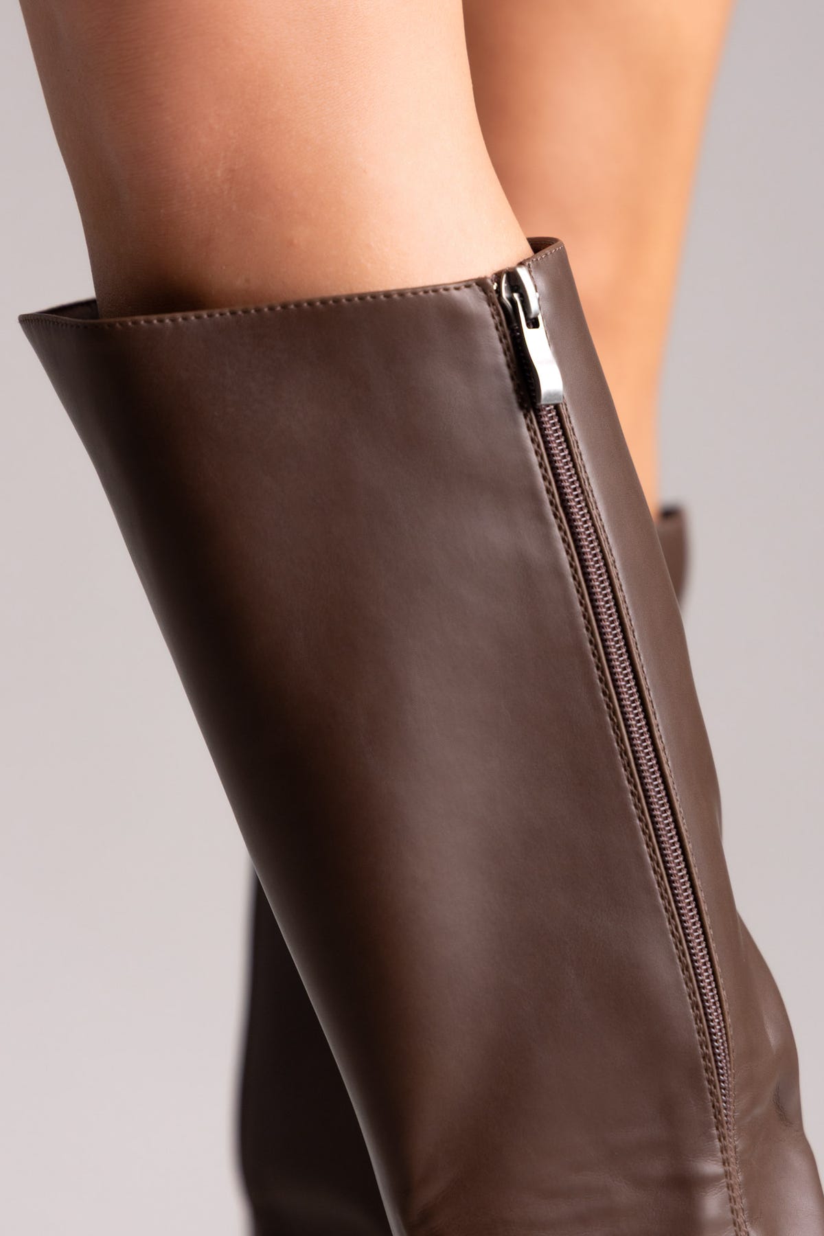 Brown leather knee-high riding boots with side zip, close-up detail of the shaft on a model
