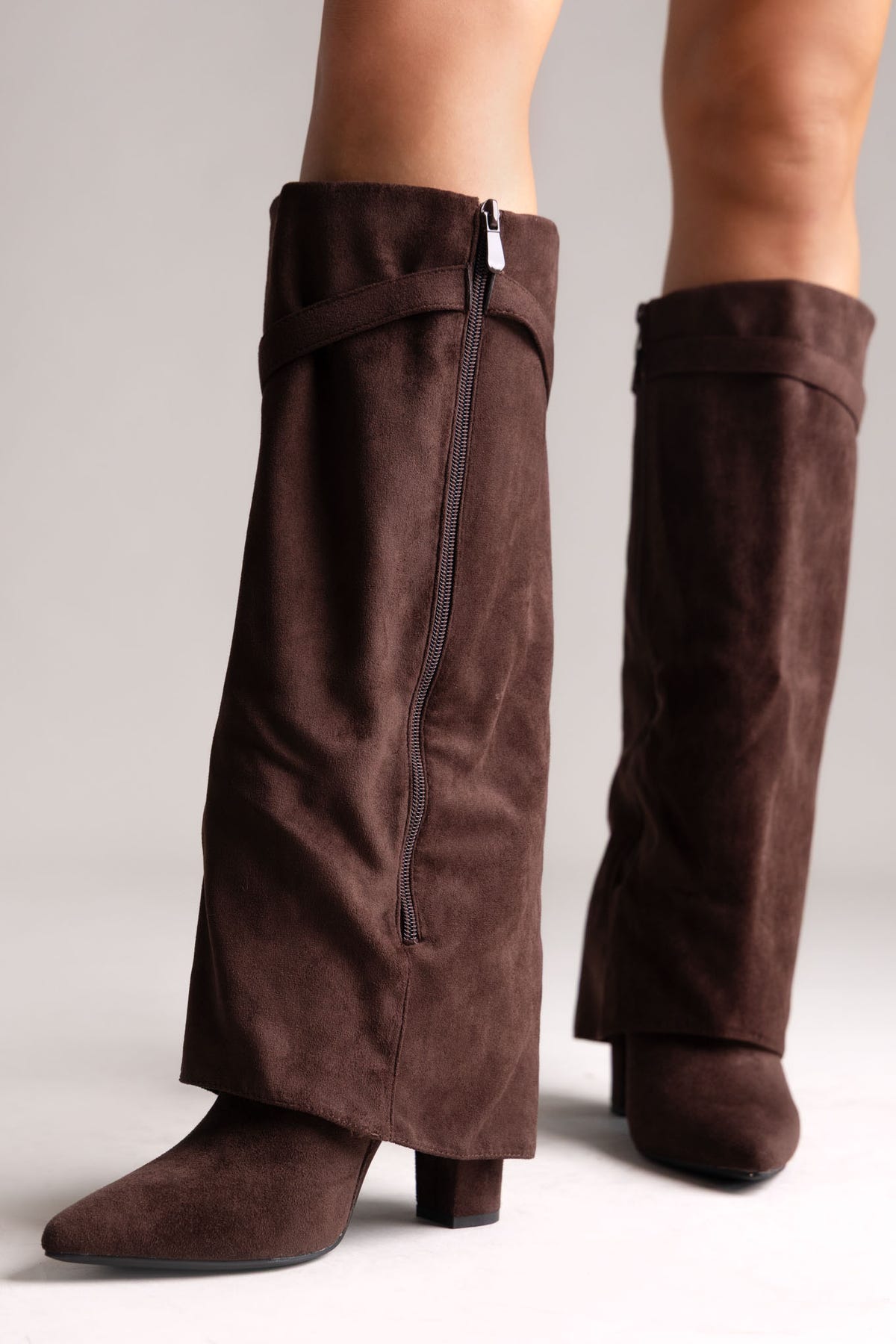 Dark brown faux suede fold-over knee-high boots with side zip and pointed toe, side view on a model