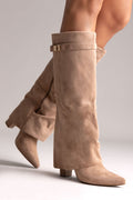 Taupe suede fold-over knee-high boots with gold buckle strap and pointed toe, angled side view on a model