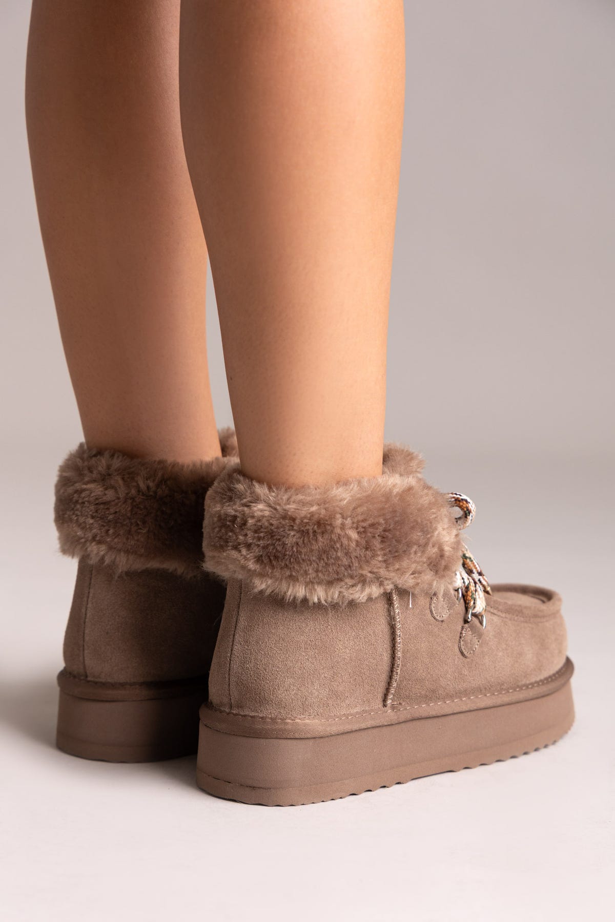Taupe suede shearling-lined platform ankle boots with chain laces and lug sole, rear view on a model