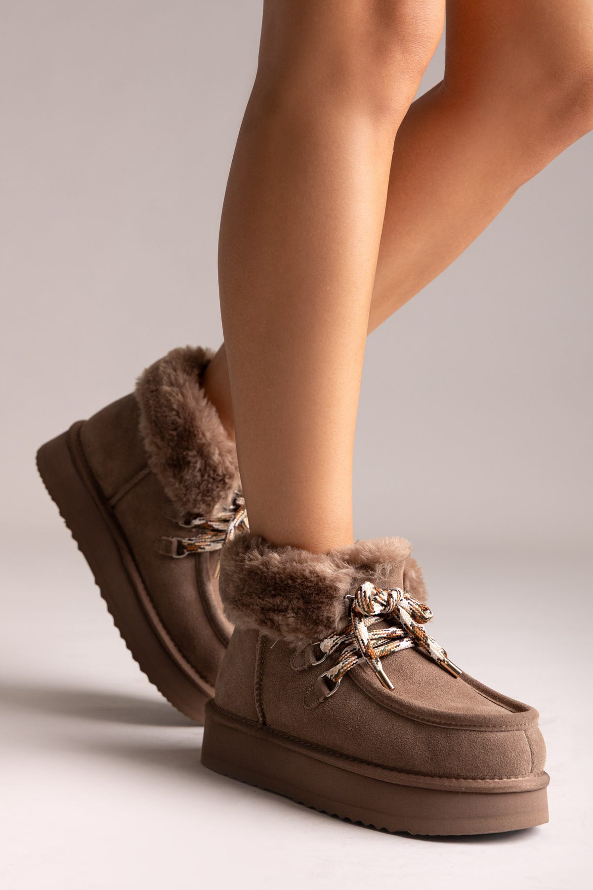 Taupe suede shearling-lined platform ankle boots with chain laces, angled view on a model