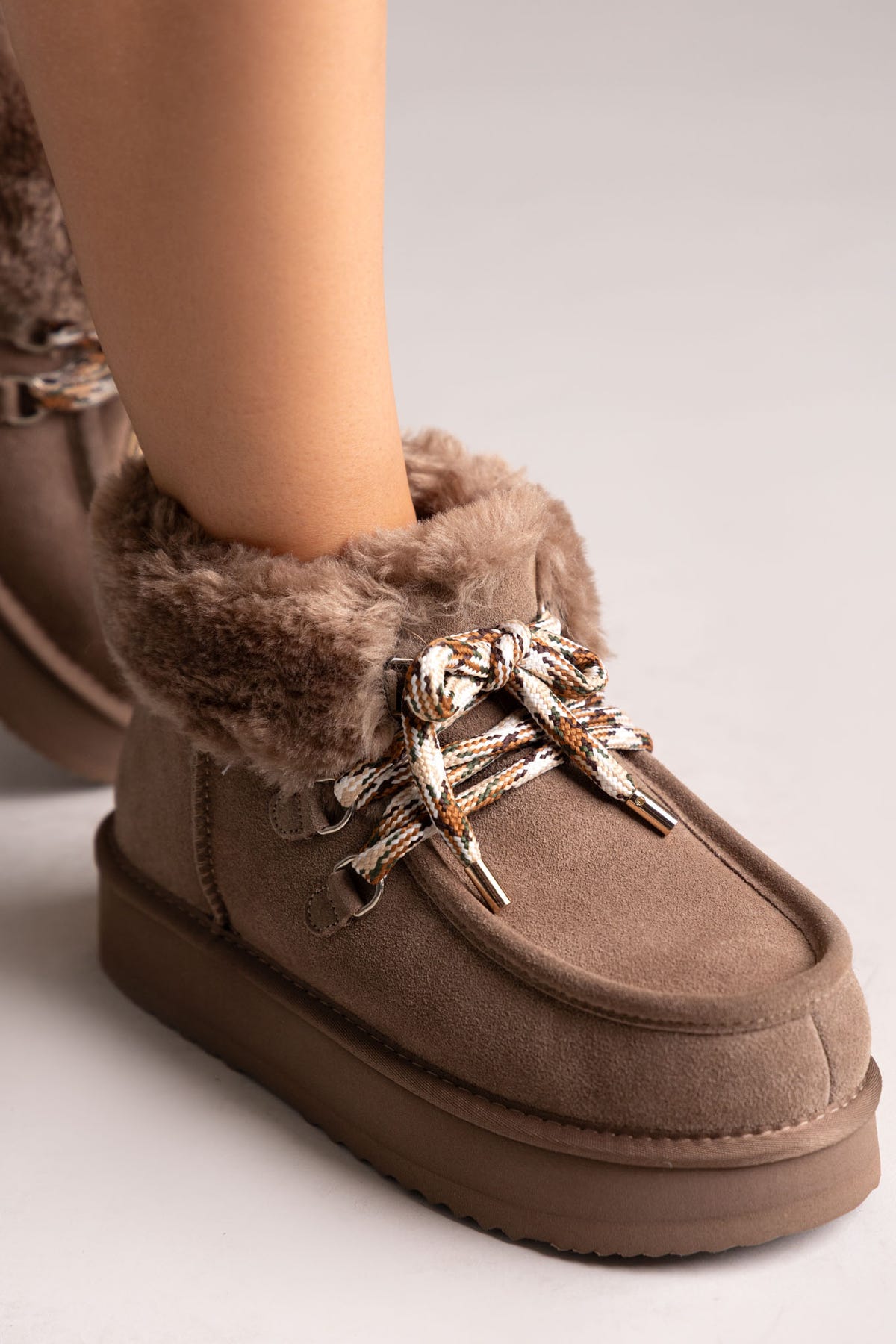 Taupe suede shearling-lined platform ankle boots with chain laces, close-up on a model