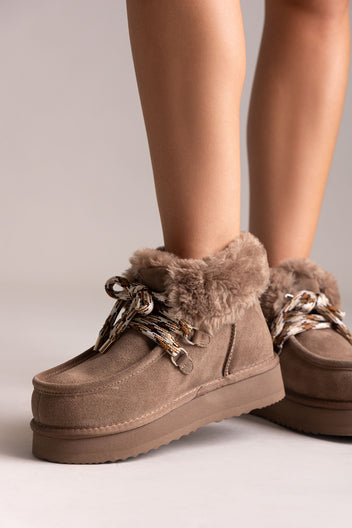 Taupe suede shearling-lined platform ankle boots with chain laces, angled view on a model