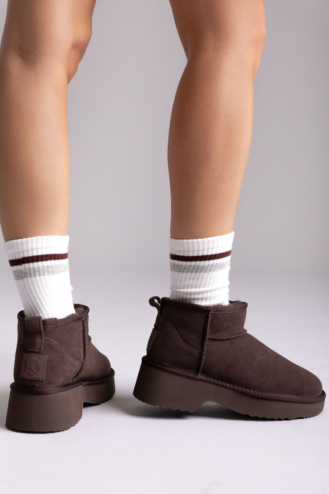 Dark brown suede platform ankle booties with striped socks, angled view on a model in studio light