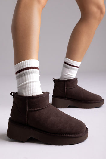 Dark brown suede shearling-lined mini ankle boots with white striped socks, side view on a model