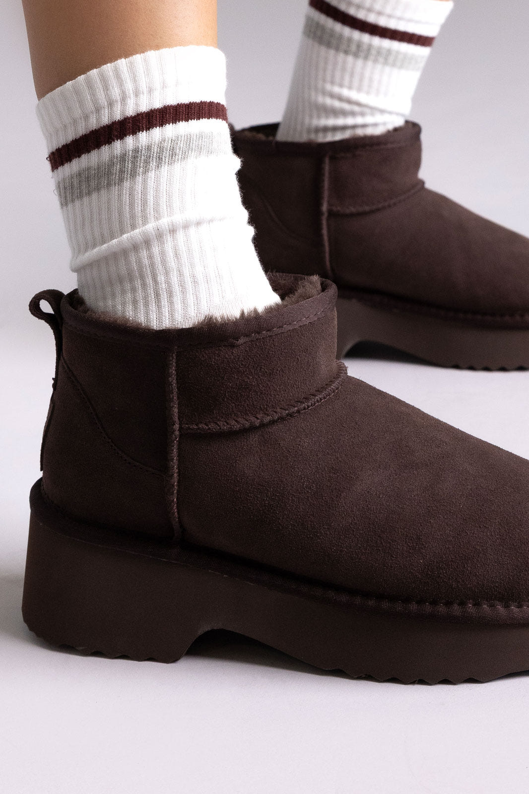 Dark brown suede platform mini ankle boots with striped socks, angled view on a model