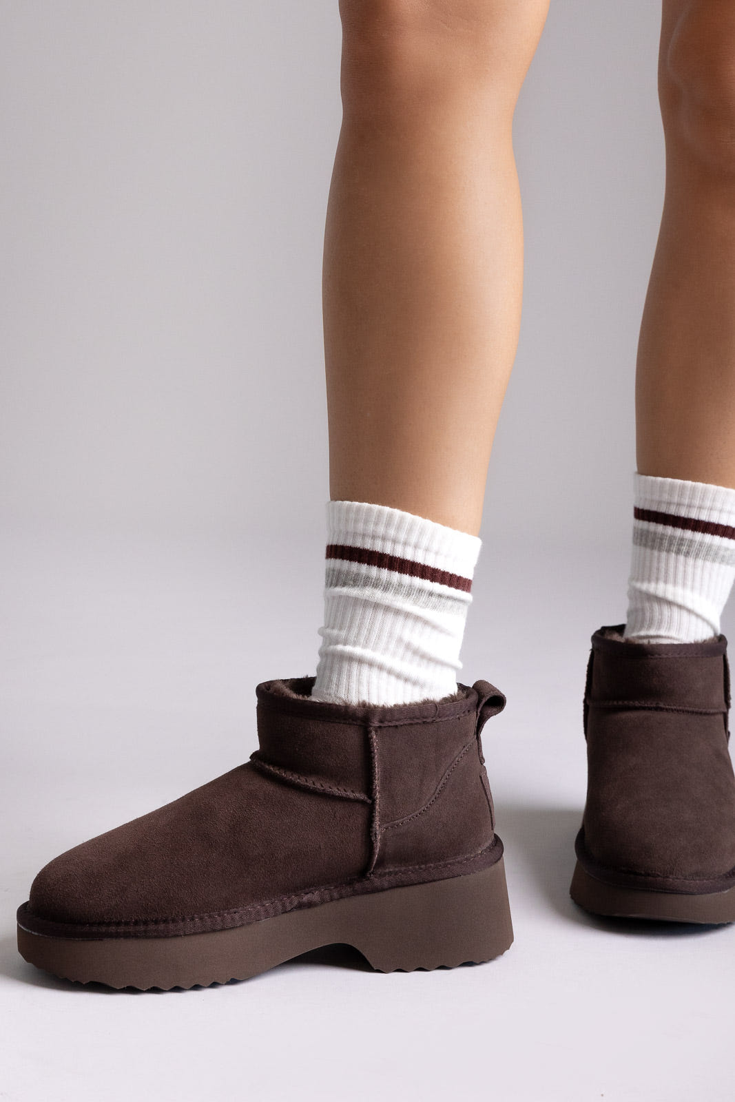Dark brown suede platform mini ankle boots with striped socks, side view on a model