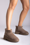 Taupe suede mini boots with fleece lining and chunky sole, side view on a model's legs in studio light