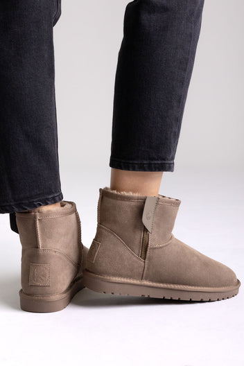 Taupe suede shearling-lined mini ankle boots with pull tab, angled view on a model in black jeans