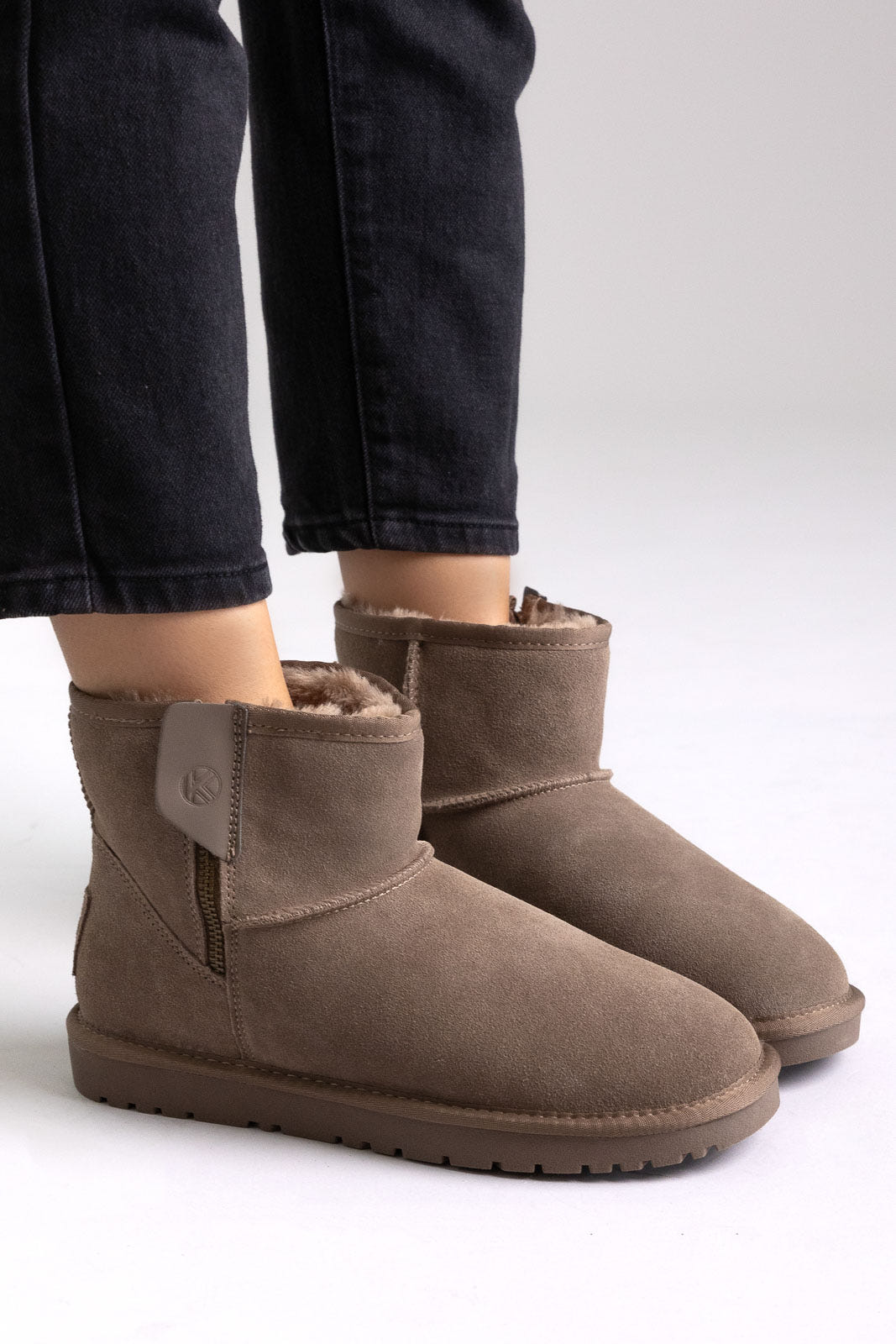 Taupe suede shearling-lined mini ankle boots with pull tab, side view on a model in black jeans