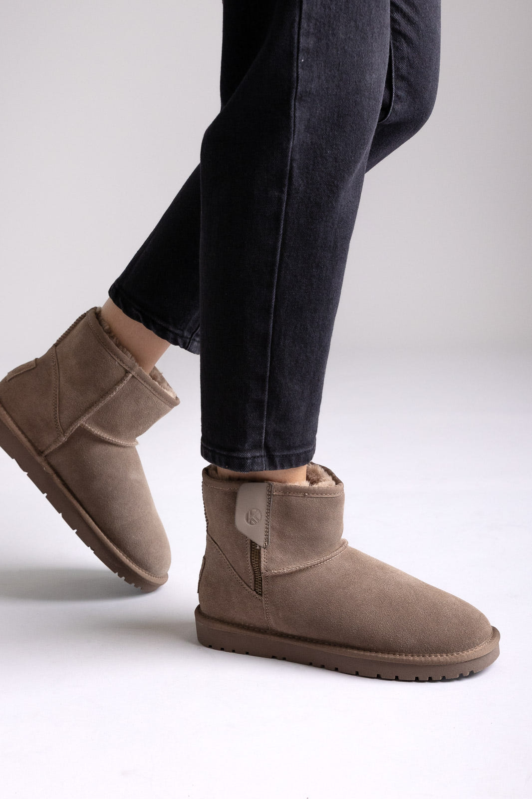 Taupe suede shearling-lined mini ankle boots with pull tab, side view on a model in black jeans