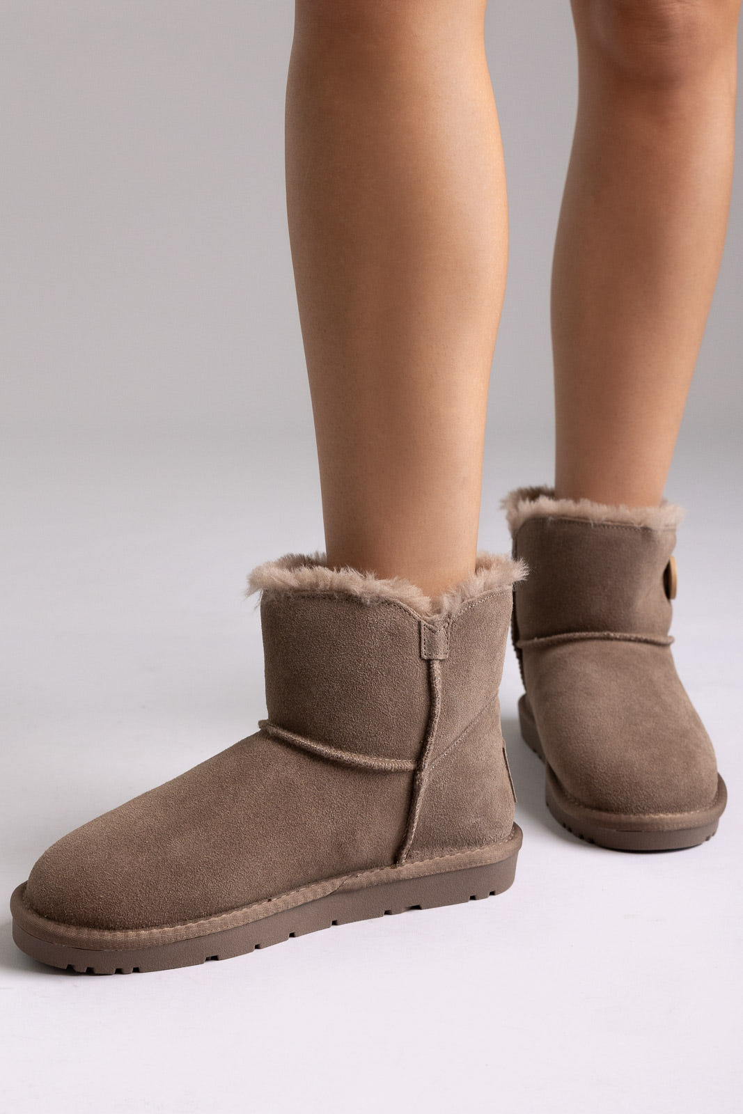 Taupe suede shearling-lined mini ankle boots with side zip, front view on a model in studio light