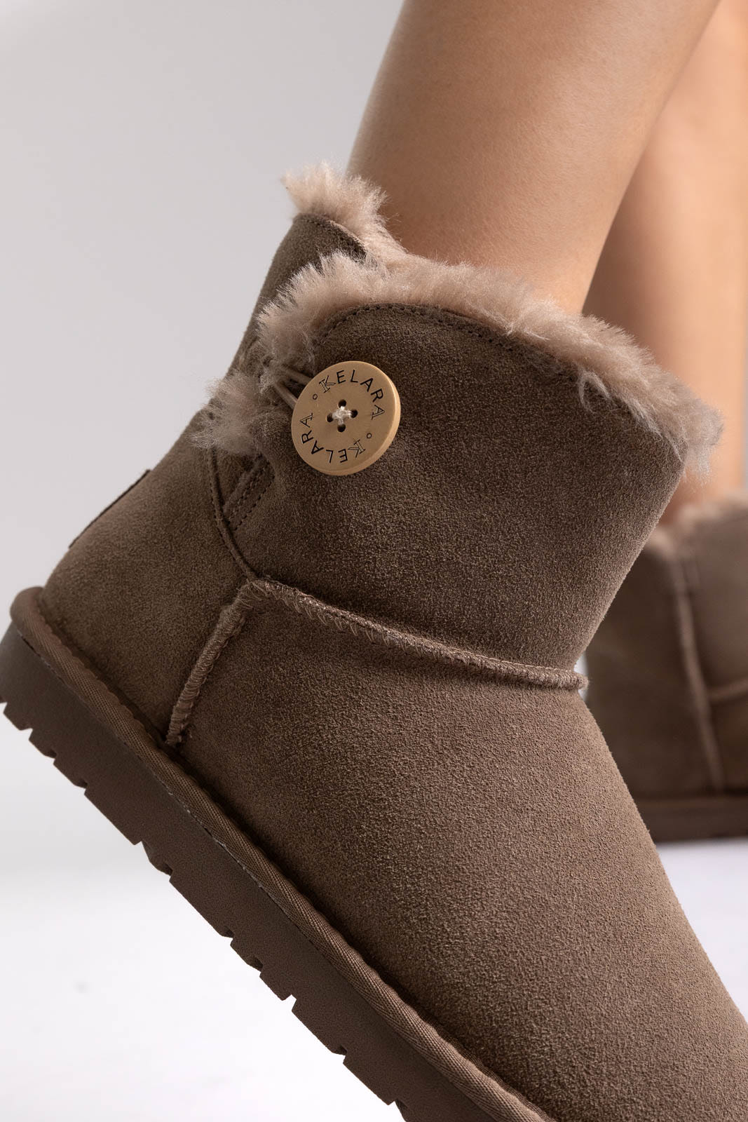 Taupe suede shearling-lined mini ankle boots with button detail, close-up on a model