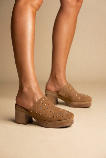 Tan suede clog-style mules with studded uppers and a chunky block heel, worn on a model, three-quarter view