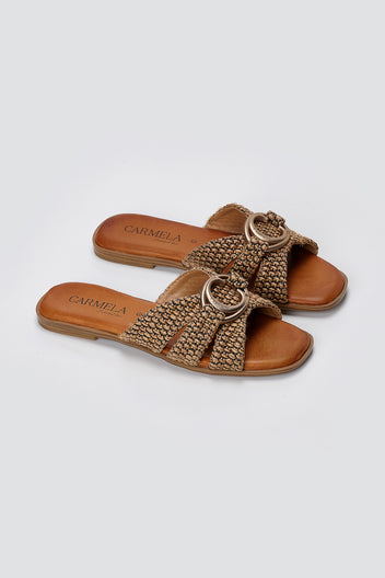 Pair of tan leather flat slides with woven crossover straps and gold ring ornament, three-quarter view