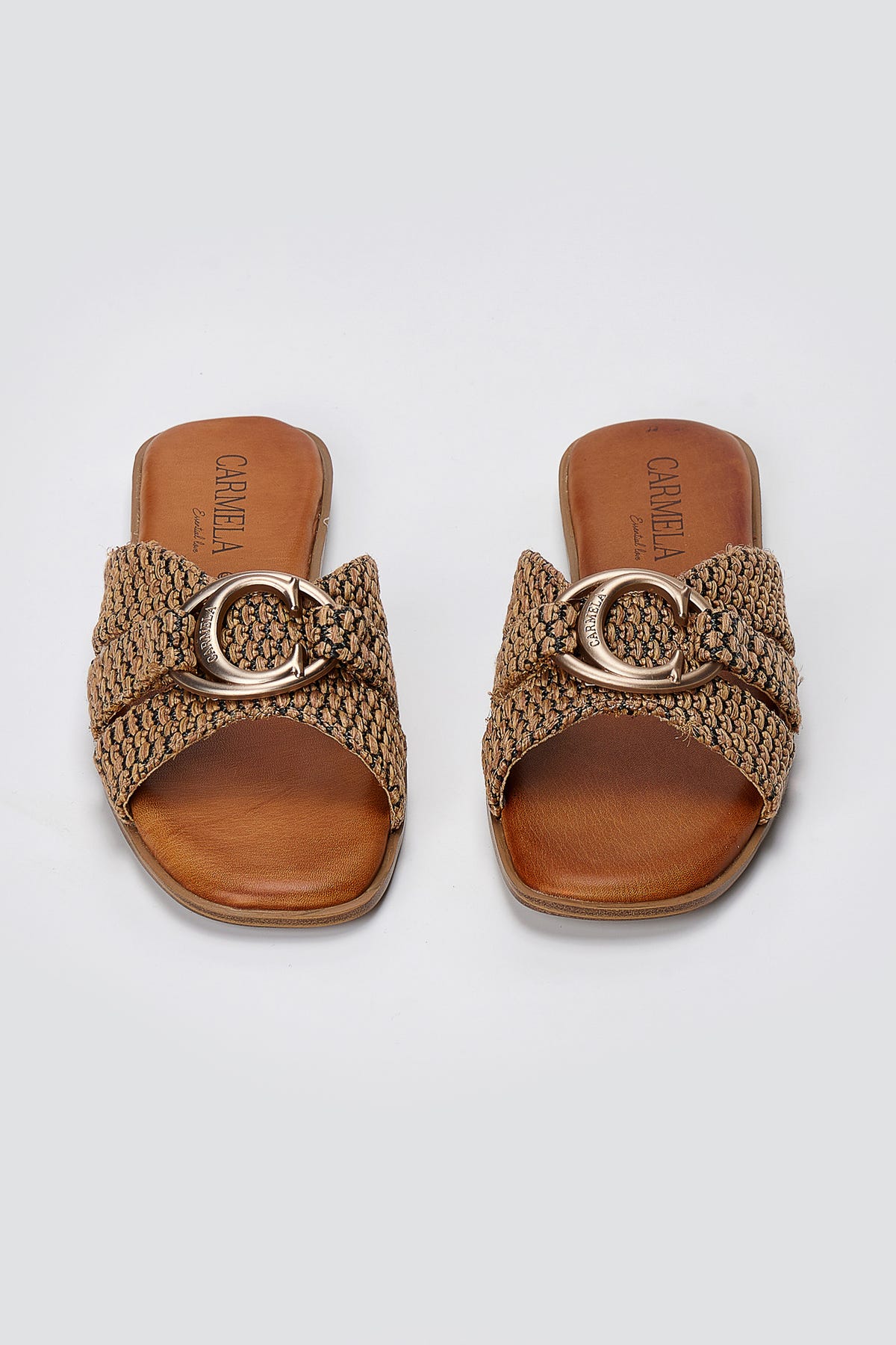 Pair of tan leather flat slides with woven knot straps and gold C-shaped ornament, top-down view