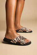Zebra print pony hair criss-cross slide sandals with silver studs and a dark brown footbed, worn on a model, side view