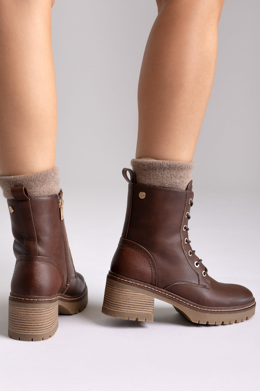 Model legs in brown leather lace-up ankle boots with chunky block heels and cuffed socks, angled view on a light backdrop